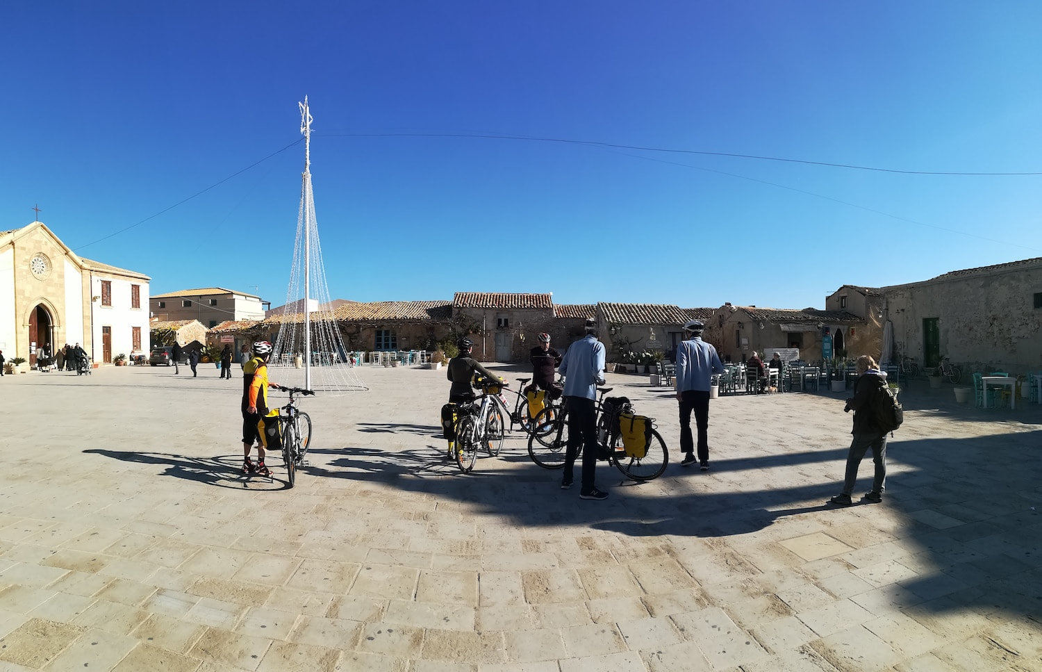 Cyclistes avec vélos et sacoches sur la place ensoleillée d'un village sicilien