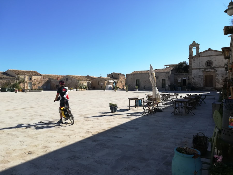 Cyclist crossing the main square of the fishing village of Marzamemi