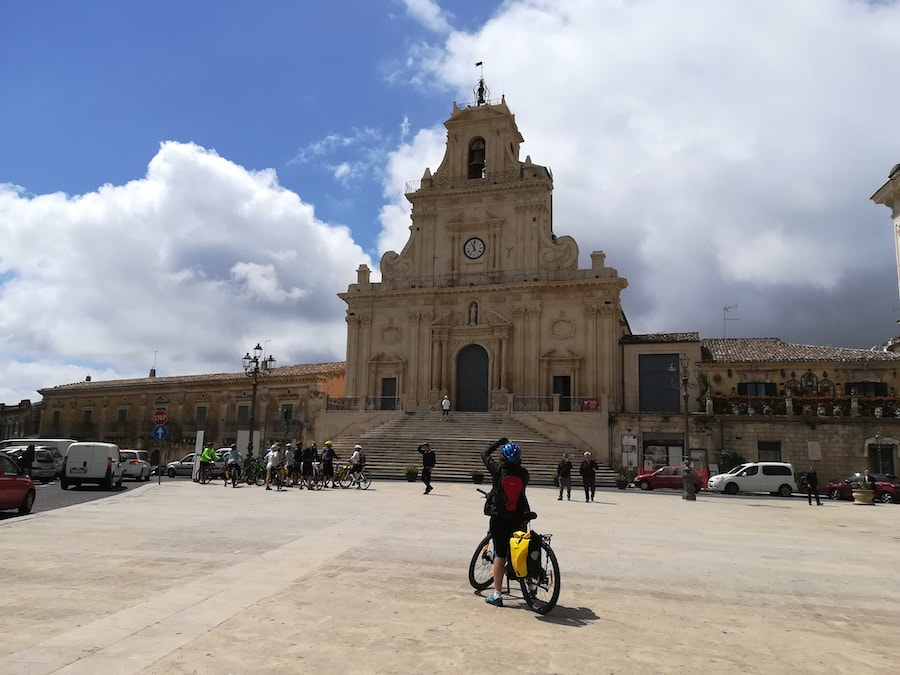 Cyclist in front of a Baroque church on the main square of Palazzolo Acreide